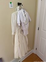 White baby boys tuxedo hanging with flower girl gown and matching hat visible behind