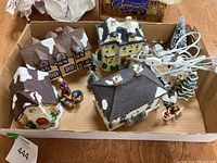 Wide overhead view of the boxed ceramic Christmas village buildings, figures, trees, and electric lights