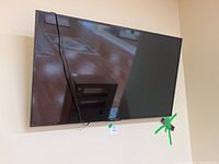 Photo of RCA Scenium 55" flat screen TV mounted on wall with cable hanging down, green tape on lower right corner near remote.