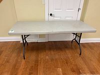 Front view of the gray plastic folding table with black legs showing surface marks and paint spots.