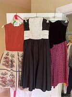 Photo showing three girls dresses hanging side by side: orange bodice with tapestry skirt, black and white Lori Anne dress, and purple velvet polka dot dress.
