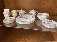 Full set of Johnson Bros Ironstone dinnerware with pink floral pattern including various plates, bowls, cups, saucers and sugar bowls displayed on a wood shelf.