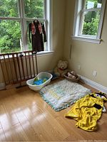 Full view of the lot showing Brownie uniform hanging, wooden pet gate on the floor, baby bath, baby quilt, basket with stuffed animals, plush teddy bear, and bumblebee towel on the floor.