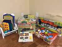 Overall view of toys, books, train set box, Kawasaki keyboard, V-Tech laptop, and toy food. Various colorful children's items shown.
