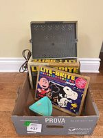 Lite-Brite box with plastic pegboard and blue stencil holder inside cardboard box.