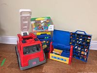 Front angle view of the Mega Bloks fire truck with open ladder, Hot Wheels case with toy cars, blue tool box, and Mega Bloks set box grouped together on floor.