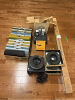 Overview of the two Kodak slide projectors alongside four slide trays and a collection of metal slide storage cases, also includes a boxed Kodak slide projection screen and manual.