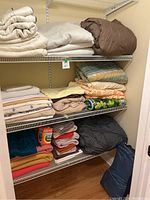 Wide view of linen and bedding items stacked on shelving including sleeping bags, blankets, towels, and a box of Bounce sheets.