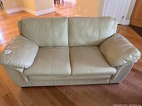 Front view of the beige pleather loveseat showing the two-seat configuration and padded armrests with visible wear.