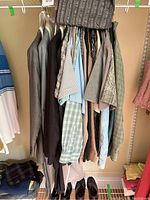 Clothing rack showing multiple men's shirts, suits, and jackets hanging, two pairs of dress shoes underneath.