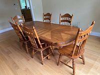 Full view of large rectangular oak veneer dining table with six matching chairs surrounding it on a hardwood floor.