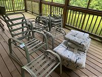 Overview of all 6 green metal folding/stacking patio chairs in a row, two matching foot stools with cushions stacked on one, and one folding aluminum chair at the side.