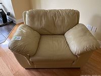 Front view of beige pleather armchair with large padded armrests and cushioned backrest.