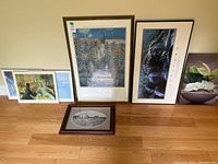 Wide shot of six framed art pieces arranged on the floor against a wall.