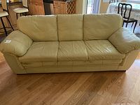 Full view of the three-seat beige/yellow pleather sofa showing cushions and overall shape.