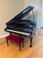 Full view of black grand piano with raised lid and matching bench on hardwood floor