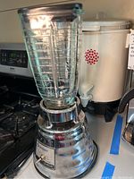 Full view of Osterizer Classic blender with glass jar on metal base near stove