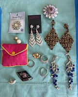 Overview of all costume jewelry items laid out on a blue cloth, showing earrings, rings, brooches, bracelet, and a pink pouch.