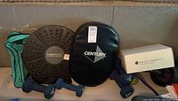 Photo showing black BodyFit balance board, Century exercise pad, boxed BeachBody dumbbell set, and multiple colored hand weights arranged together.