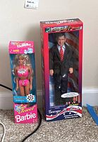 Photo showing both boxed dolls together, George W. Bush talking doll and Sun Jewel Barbie doll side by side on floor.