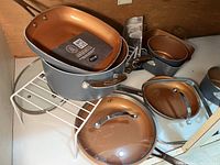 Cookware items including pots, pans, glass lids, and detachable handle arranged clustered together.