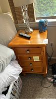 Wooden nightstand next to a bed showing the full piece with four drawers and items on top.