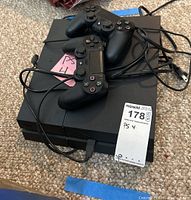 Sony PS4 console with two wired DualShock controllers and cables on carpeted floor.