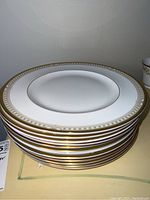 Stack of 12 Royal Doulton Lichfield pattern dinner plates showing the decorative golden and green border with beaded edge detail.