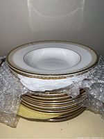 Stack of white Royal Doulton soup bowls with gold and soft colored pattern borders, shown wrapped in protective bubble wrap.