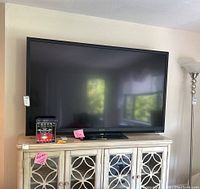 Front view of the large Sharp flatscreen television on a stand in a room with beige walls and a lamp nearby.