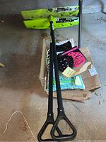 Two Steel Core snow shovels with 24-inch blades, green plastic blade, black shaft with triangle grips lying on floor.