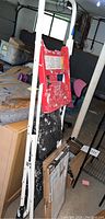Full view of metal step ladder with white frame and red steps, covered with paint stains, standing upright in a cluttered workspace.