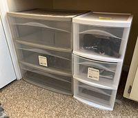Two plastic 3-drawer storage containers side by side with content not included, against wall on floor.