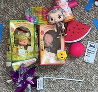 Overview of Strawberry Shortcake dolls boxed and assorted toys including pinwheel, pop-it, watermelon slice, pink ball, camcorder, and Funko Pop figure
