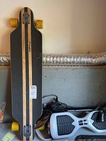Black and natural wood Rimable longboard skateboard leaning against a wall next to white and black Swagtron smart board hoverboard and black charger/pump.