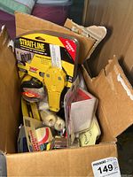 Box containing various tools including a packaged Strait-Line laser level and stud finder, measuring tape, screwdrivers, and other small tools.