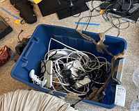 Blue storage bin filled with assorted Wii remotes, cords and accessories wired tangled inside.