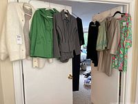 Wide angle of hanging dress clothing on door frame including sweaters, jackets, dresses in assorted colors and styles