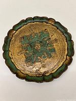 Top-down photo of old Italian decorative tray with gold and green scrollwork, showing wear and fading.