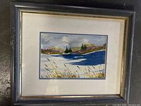 Framed watercolor painting featuring a lake, trees, hills, and sky with a foreground of tall grass.