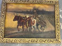 Full front view of oil painting depicting two oxen pulling a log-laden cart driven by a man, set in a field at dusk, in ornate gilded wood frame