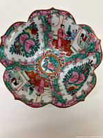 Top view of painted porcelain bowl with scalloped edge showing hand-painted floral patterns and figures in traditional dress, highlighting color and design detail.