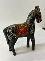 Side angle of vintage wooden horse figurine showing ornate painted decorations and saddle detail.