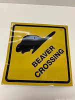 Front view of square yellow metal sign showing black beaver silhouette and 'BEAVER CROSSING' text in black.