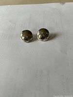 Photo of a pair of silver round earrings with embossed floral pattern on a plain background.
