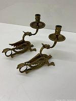 Pair of brass gryphon candle holders shown from the side angle, displaying detailed sculpted gryphons each holding a single candle socket.