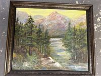 Full view of the framed landscape oil painting showing pine trees, river, and mountains, with signature visible in the lower right.