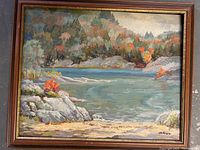Full view of seascape oil painting on board, showing the shoreline, water, rocks, and autumn-colored trees in the background with artist signature.