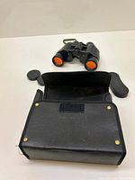 Binoculars with protective lens caps and black carrying case laid out on white surface.