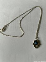 Photo showing sterling silver necklace with chain and Hamsa hand pendant with blue stone detail.